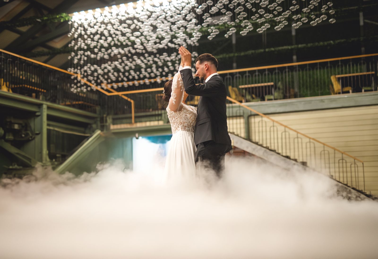 Couple dancing inside low fog under warm festoon lights.