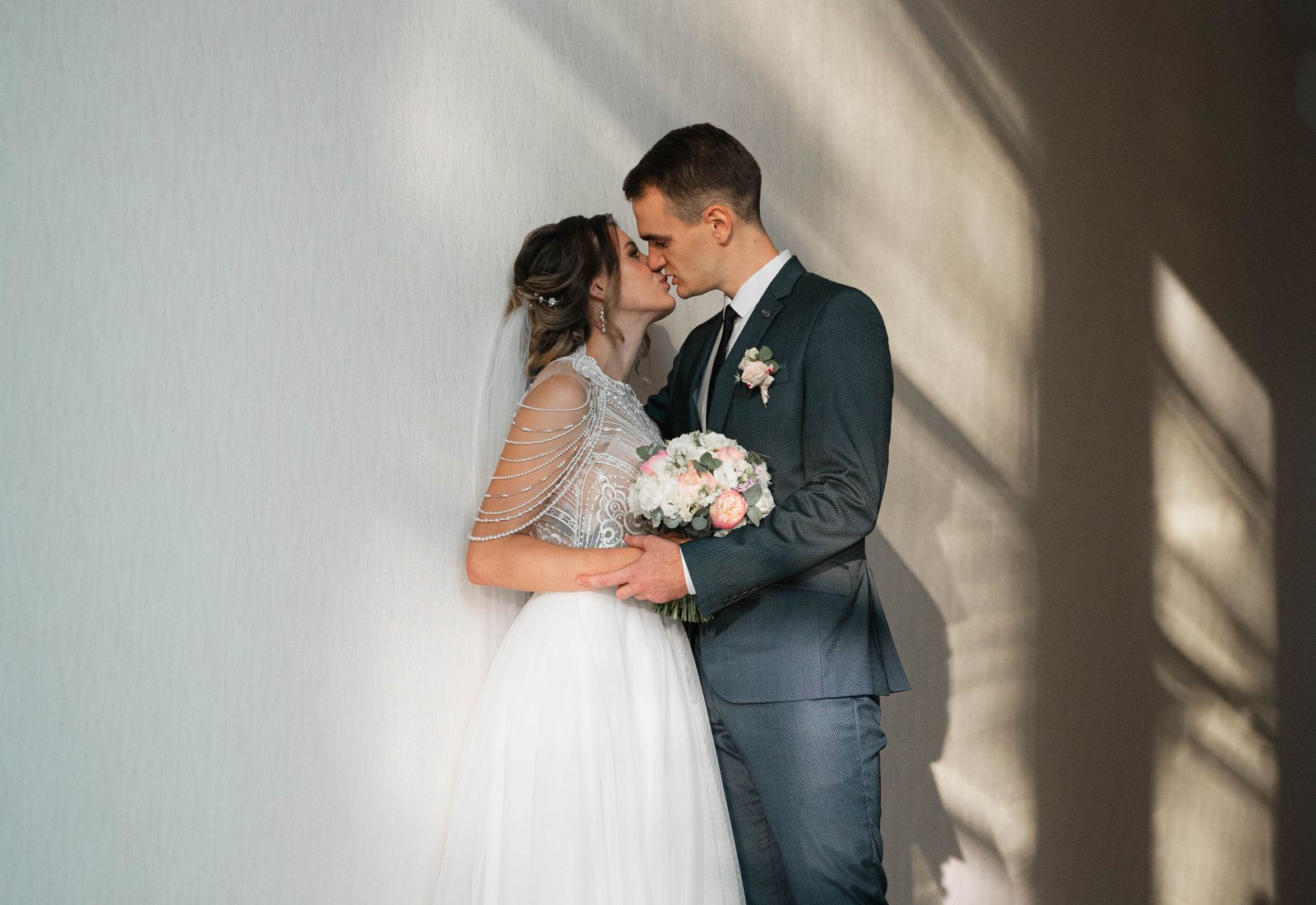 Couple standing close in a bare room crossed by window light.