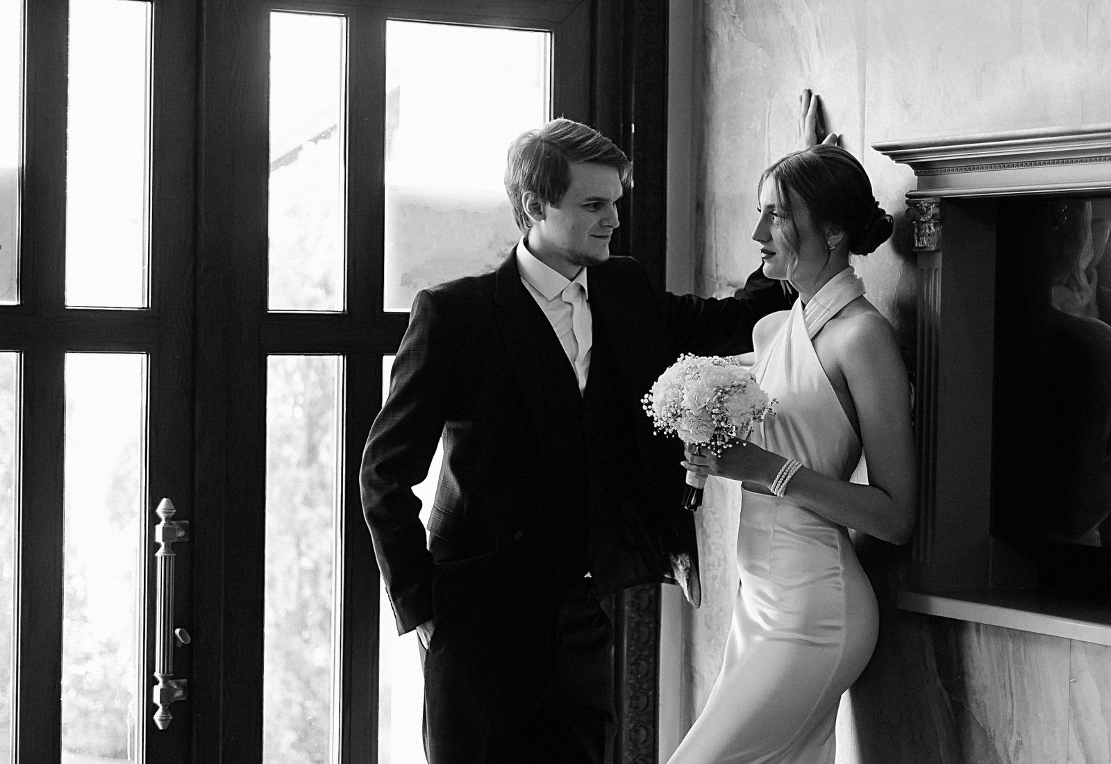 Bride and groom framed by a tall arched window.